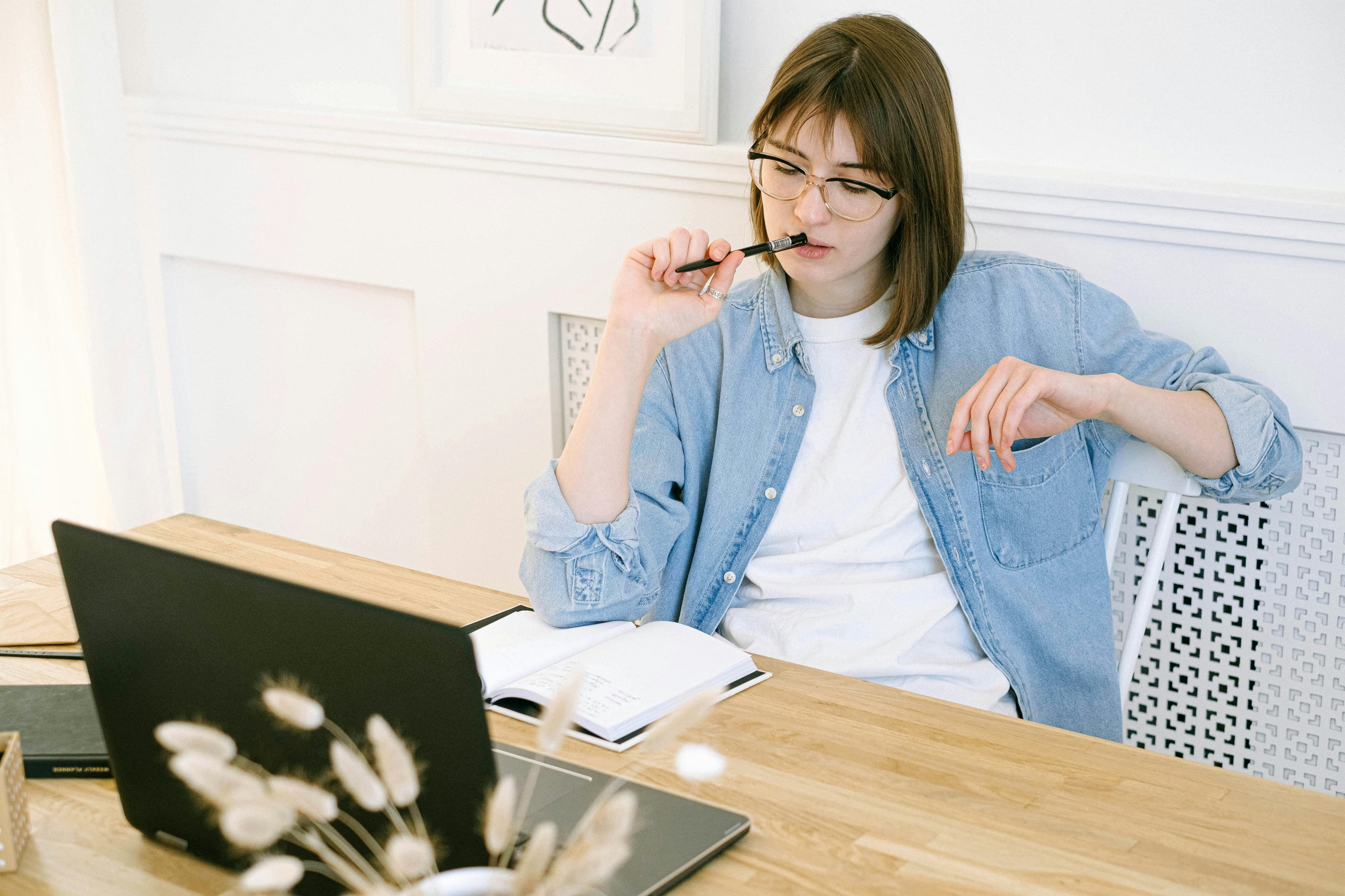 Woman contemplates her writing at the desk with a laptop and a journal.