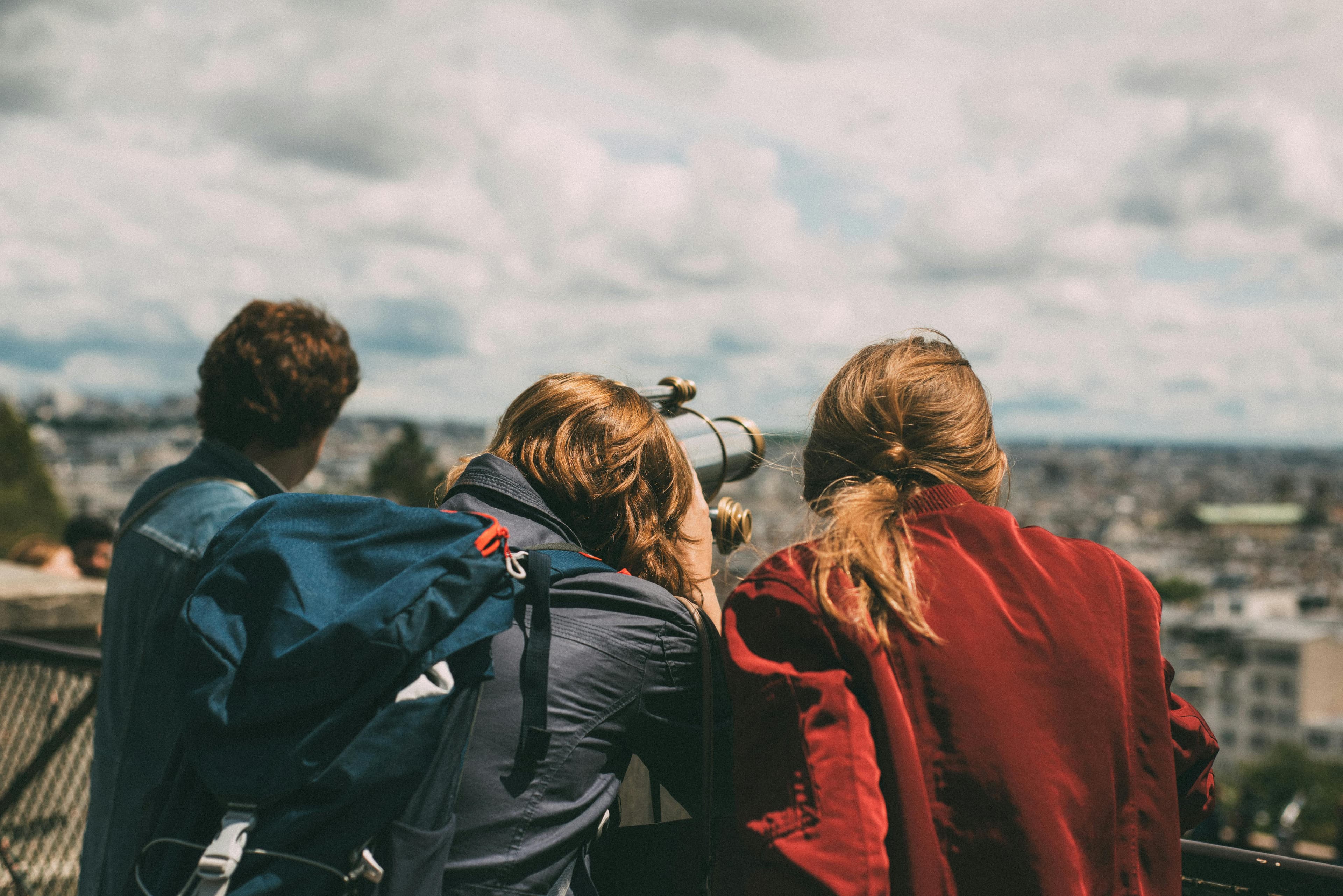 Three people look over a fence with a telescope.